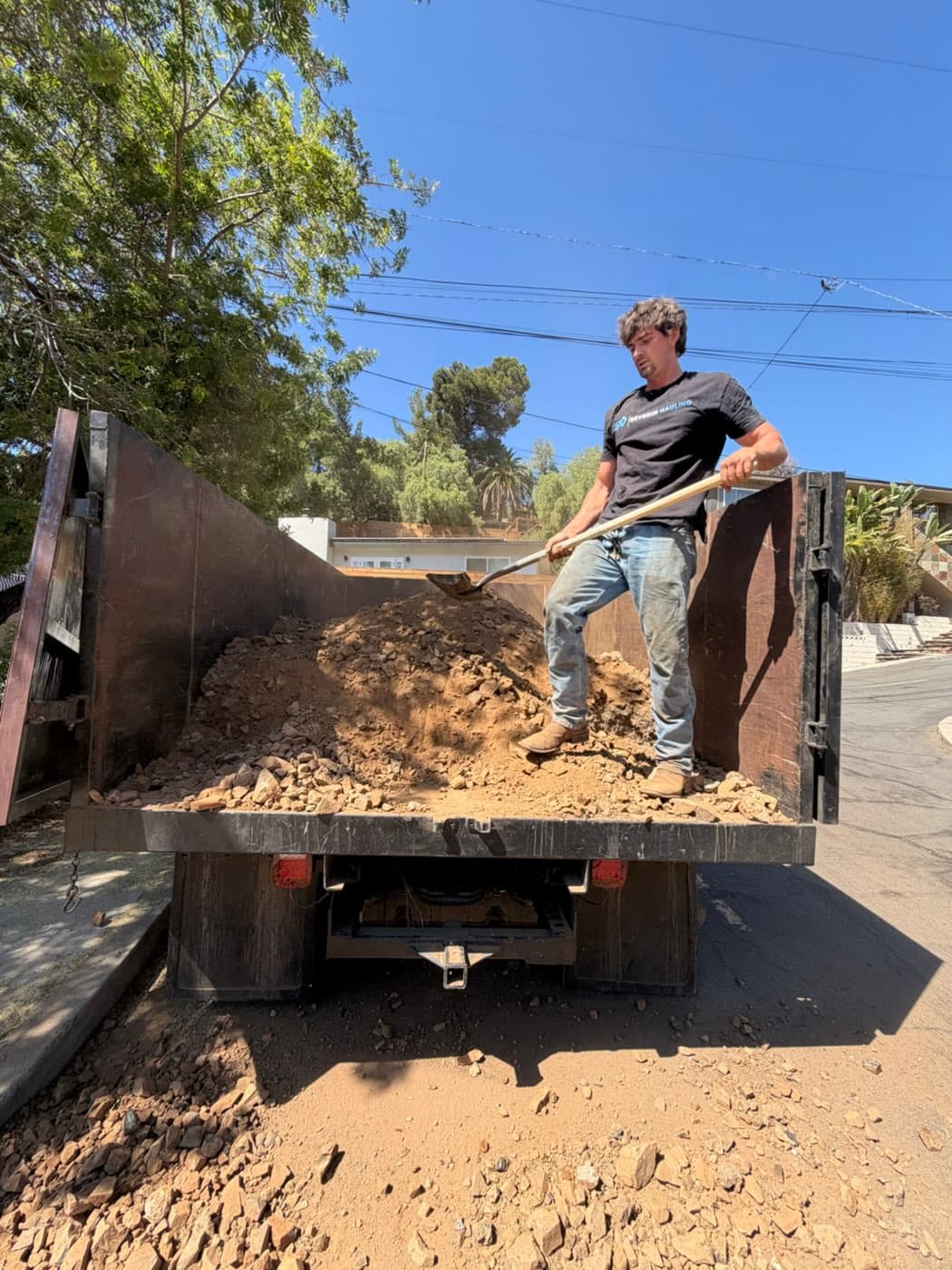 Severin Hauling crew member shoveling excavated dirt and rock in a dump truck bed in La Mesa