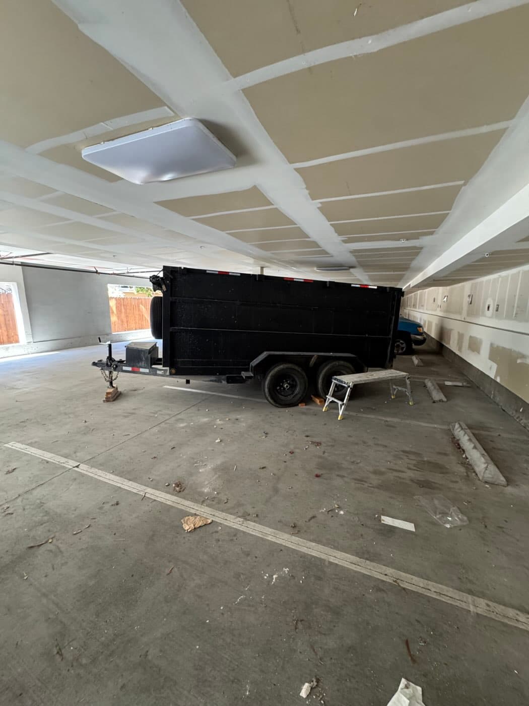 Black dump trailer parked inside a low-ceiling apartment parking garage in North Park, San Diego